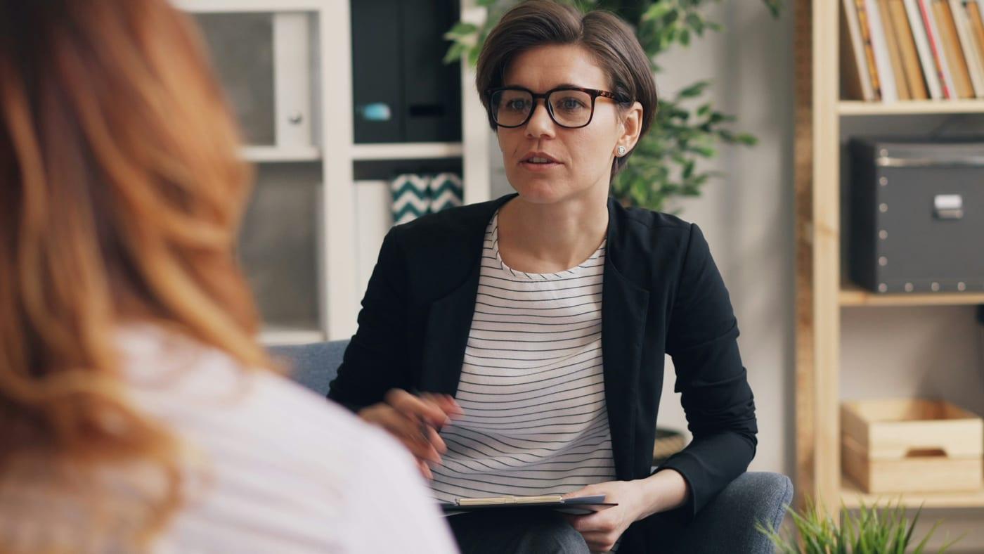 Eine Person mit Brille sitzt einer anderen im Gespräch gegenüber und hört aufmerksam zu.