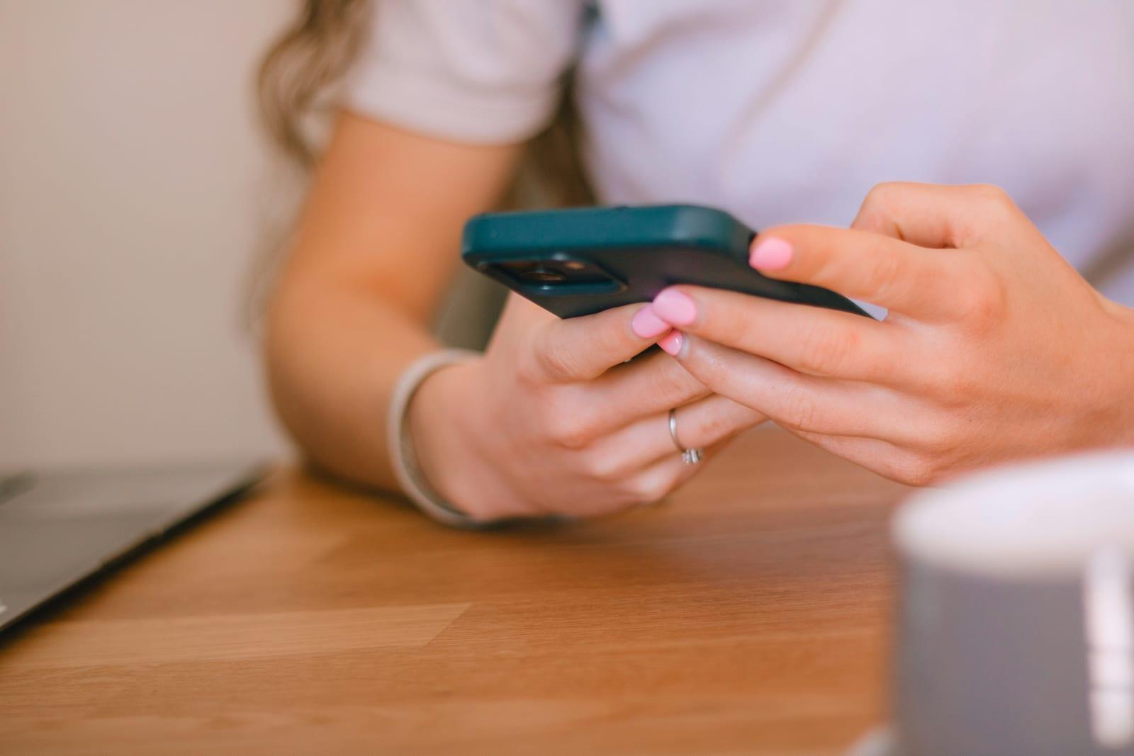 Nahaufnahme: Eine Person hält am Tisch ein Smartphone in beiden Händen.